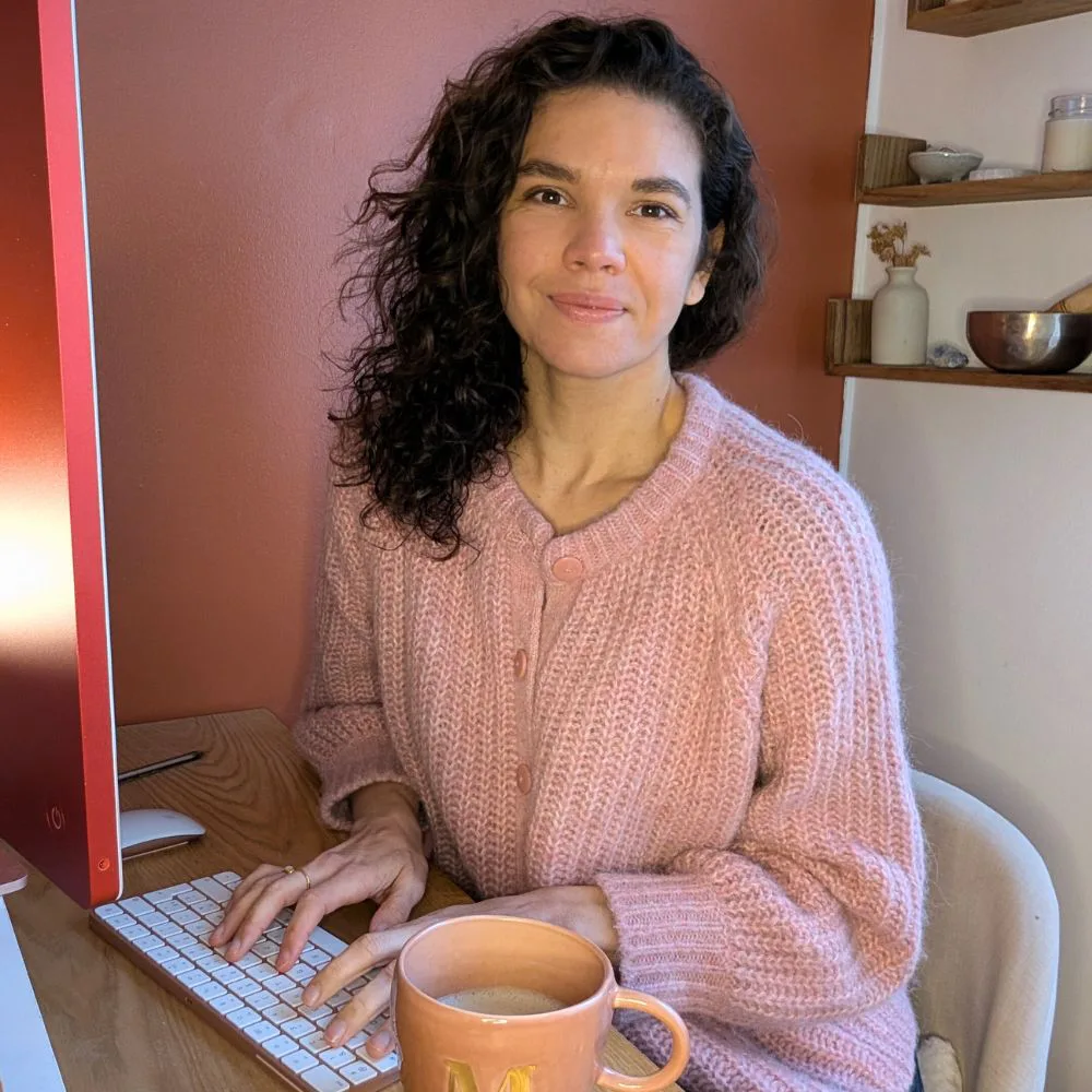 Mélissa Tellaa, thérapeute en analyse transgénérationnelle, souriante à son bureau, les mains sur le clavier et une tasse à côté